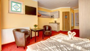 Habitación de hotel con cama, dos sillas, una mesita, televisor, un cuadro, microondas y una puerta de madera.