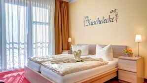 Habitación de hotel con cama, dos mesitas de noche, lámpara de pared, frutera y un ventanal con cortinas.