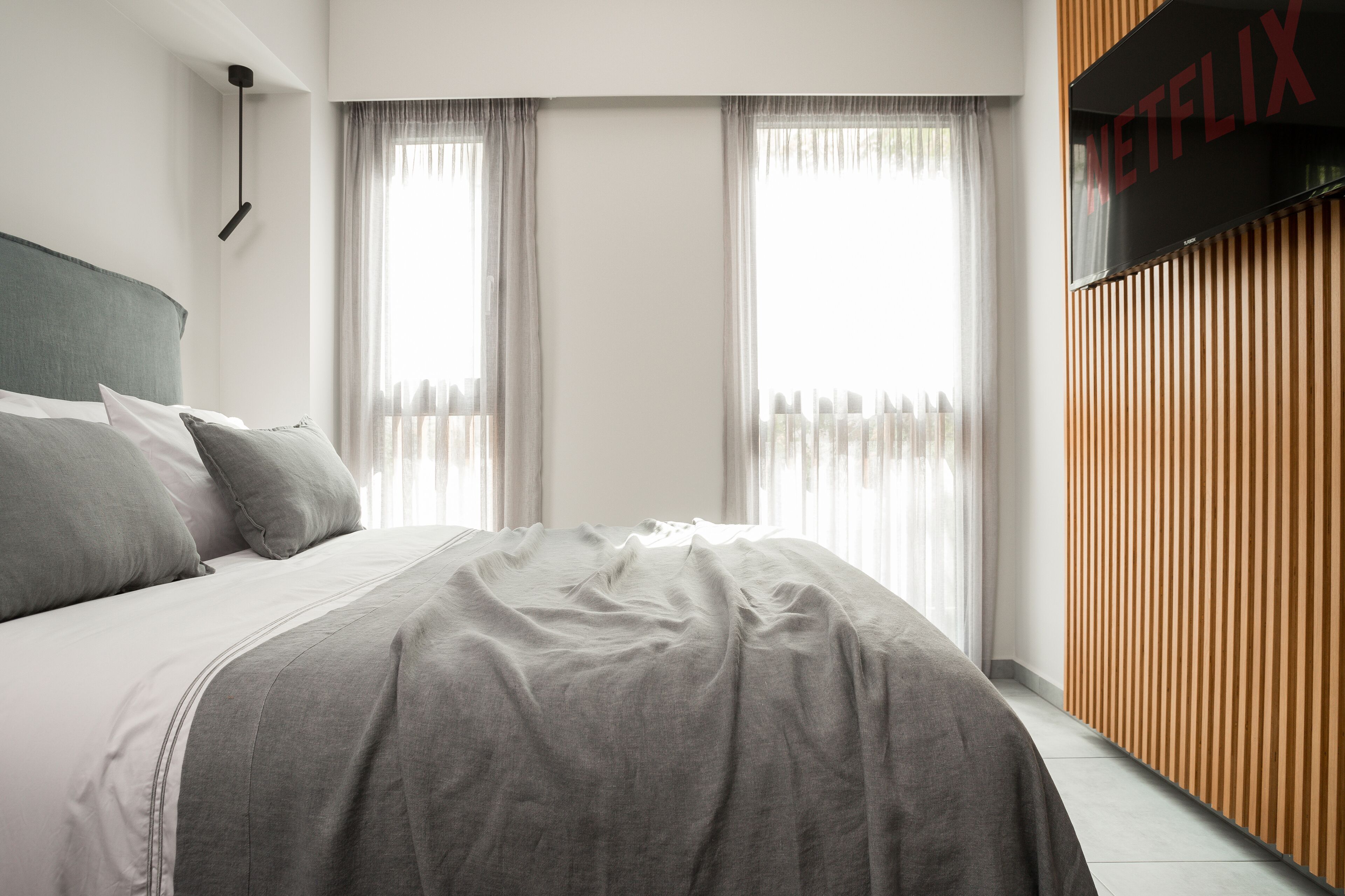 A modern bedroom with a bed, curtains, a wall-mounted TV, and a wooden panel wall.