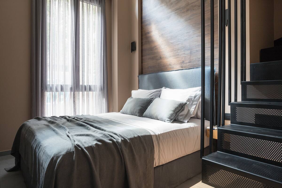 Une chambre à coucher moderne avec un grand lit, une tête de lit en bois et un escalier doté d’une rampe en métal.