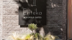 Une enseigne pour l’hôtel Enteka Acropolis Suites, avec un mur de pierre en arrière-plan et une petite composition florale devant.