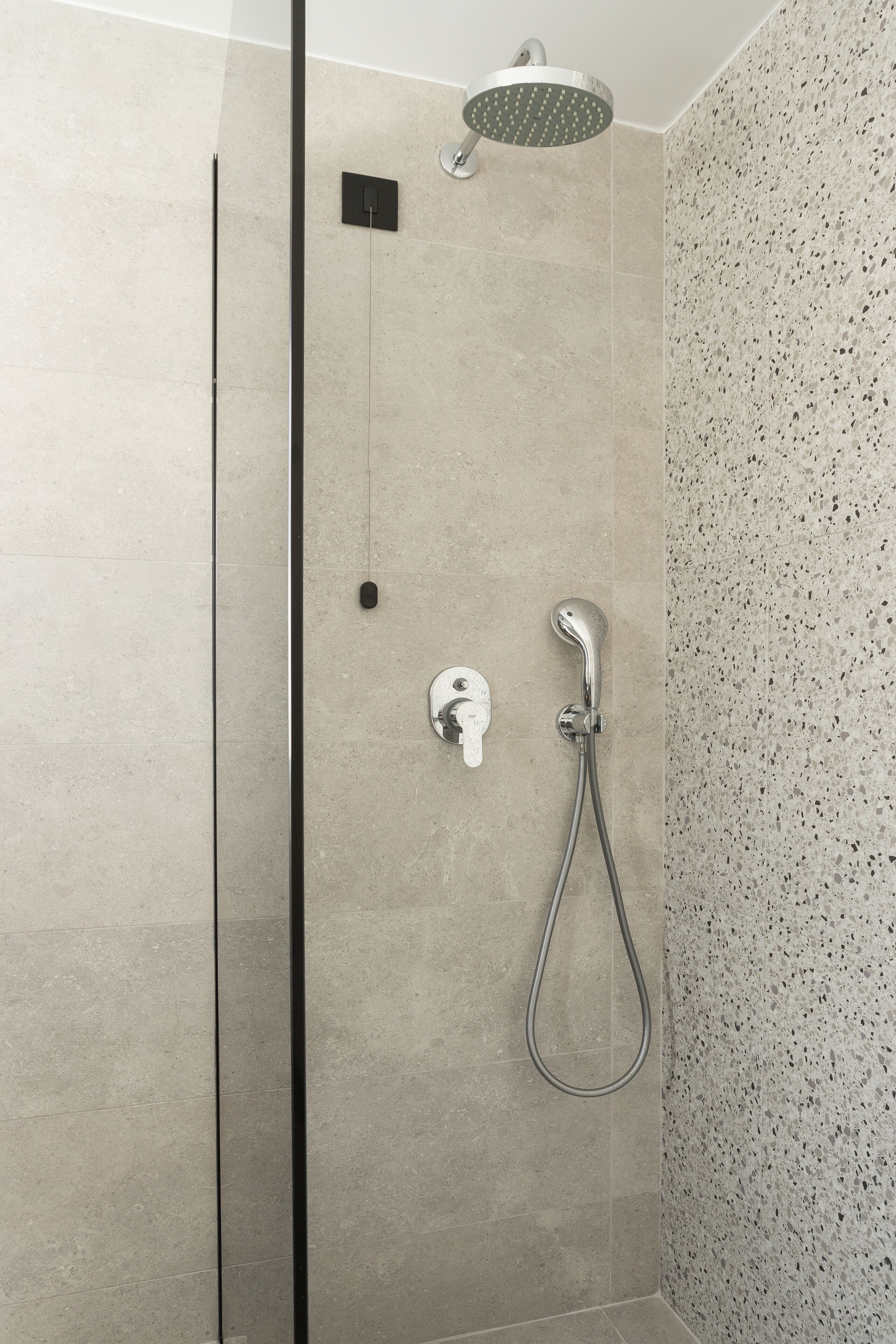 A modern shower with a handheld showerhead and a wall-mounted control.