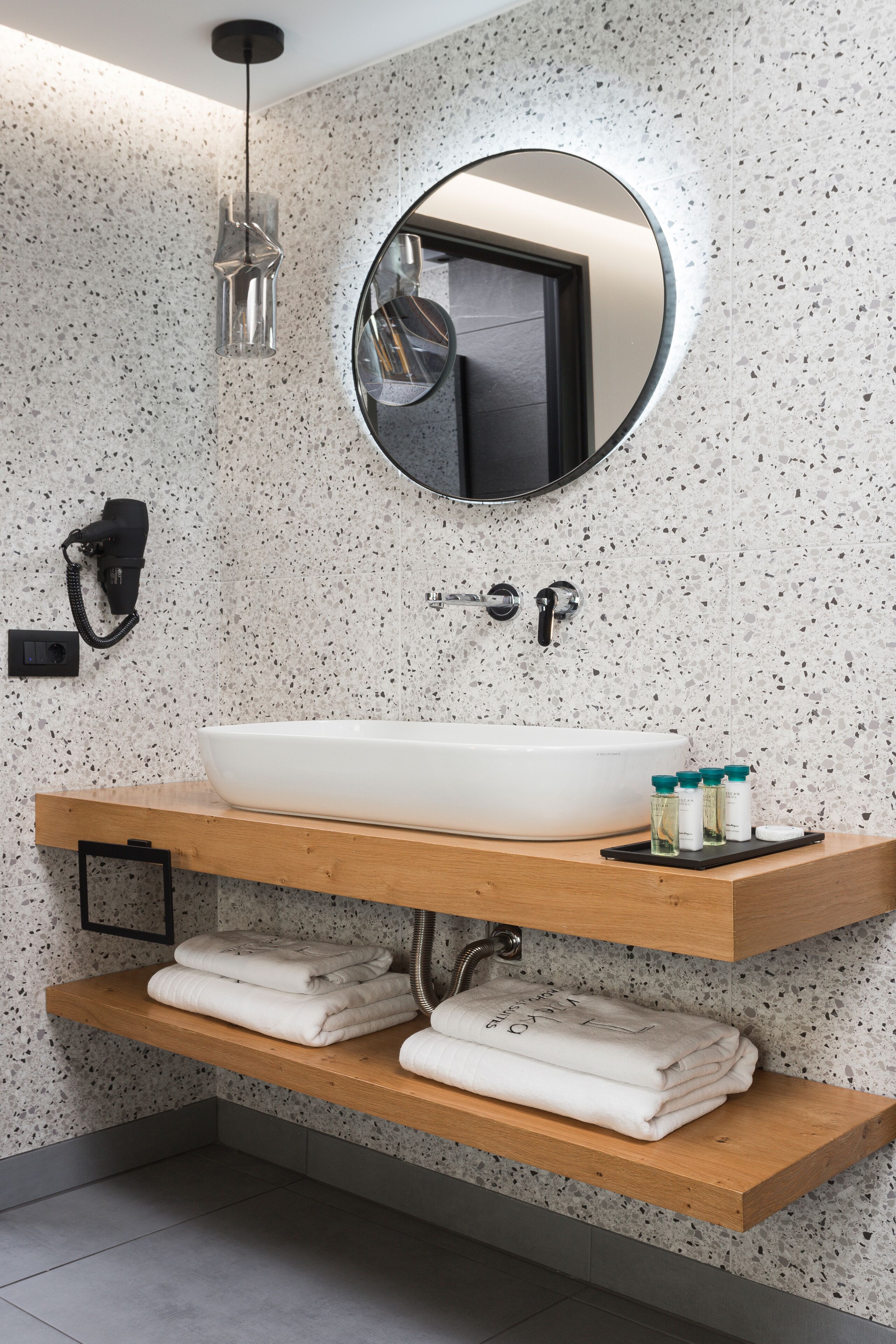 A modern bathroom with a freestanding sink, a round mirror, and built-in shelves for towels and toiletries.