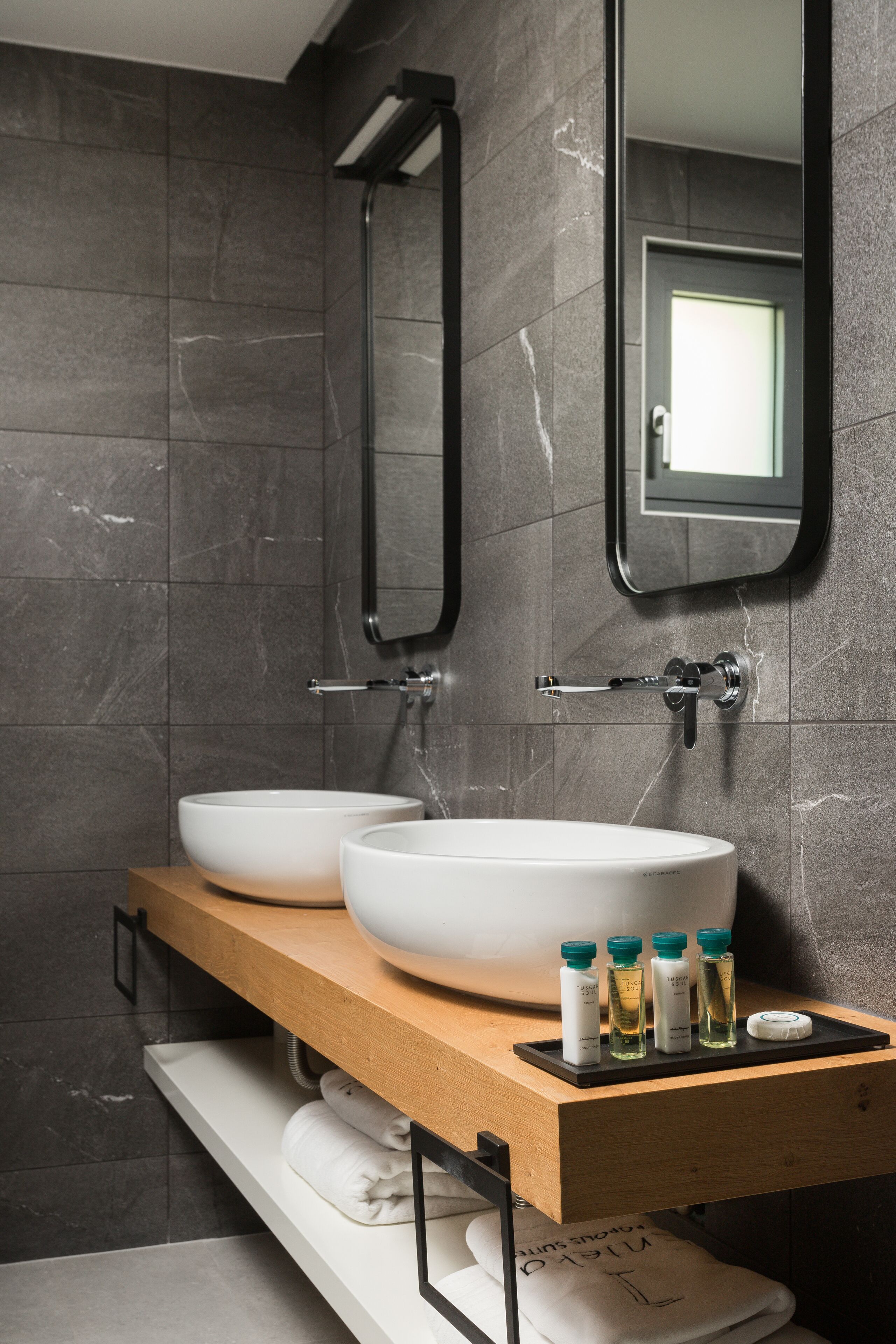 Un baño moderno con dos lavamanos grandes de color blanco, un mueble de tocador de madera, un perchero para toallas y un espejo.