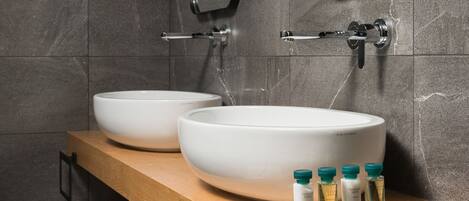 Un baño moderno con dos lavamanos grandes de color blanco, un mueble de tocador de madera, un perchero para toallas y un espejo.
