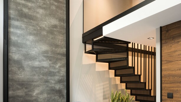 Un salon moderne avec un canapé gris, deux petites tables rondes, un escalier avec des éléments en bois et un luminaire suspendu.
