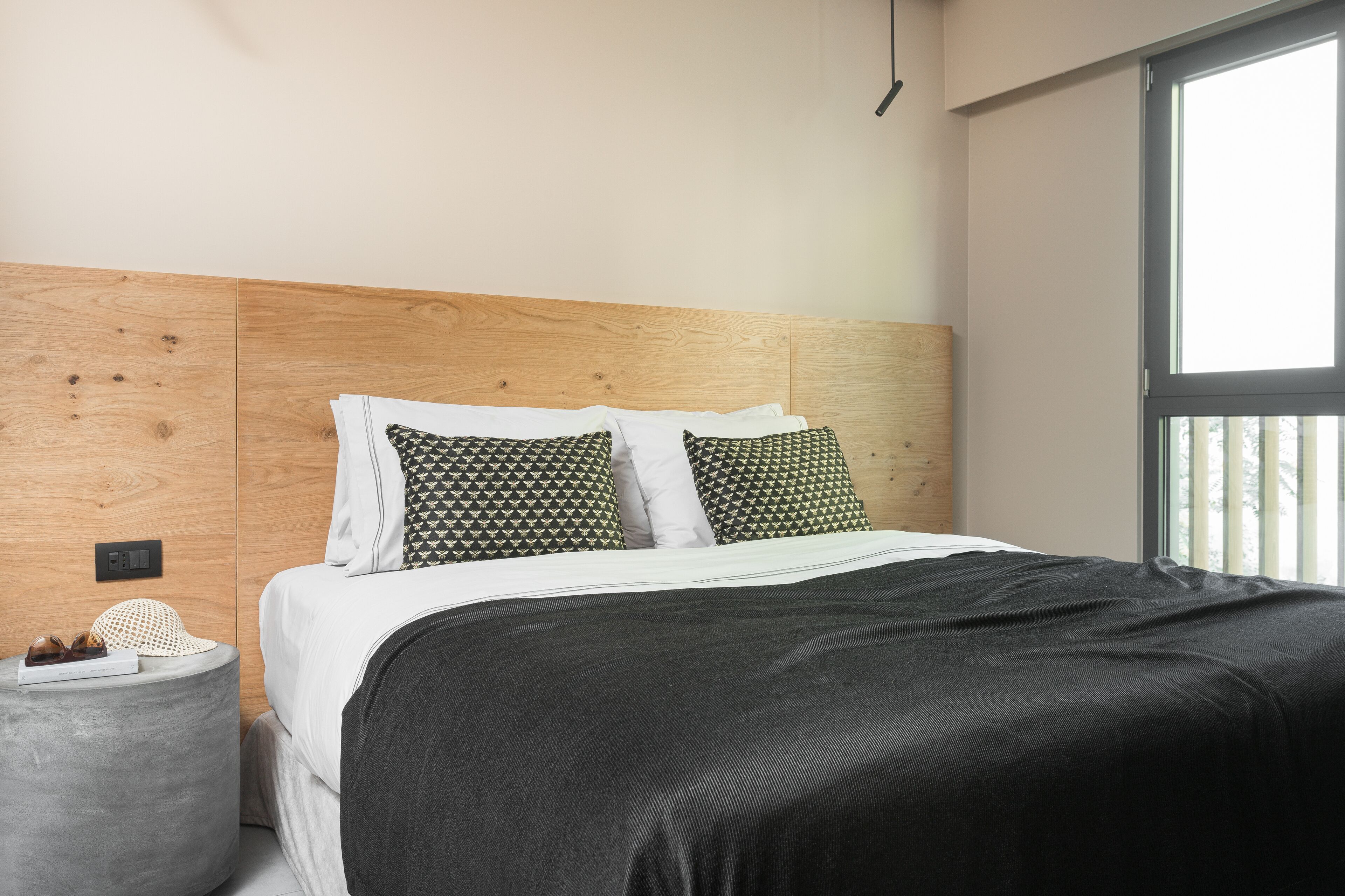 A modern bedroom with a wooden headboard, a black bedspread, and patterned pillows.