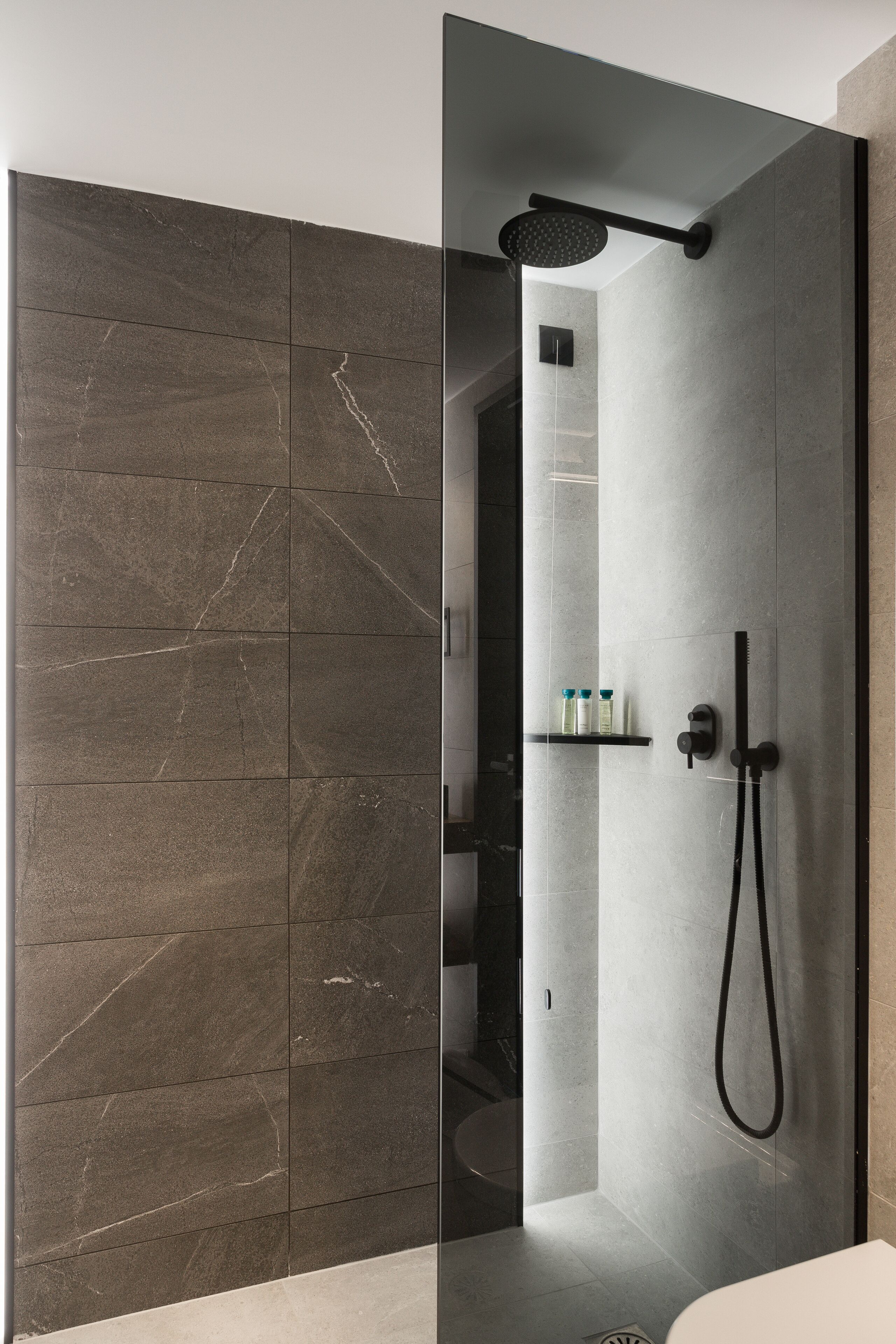 Un baño moderno con cabina de ducha de vidrio, cabezal de ducha manual negro y grifo empotrado en la pared.