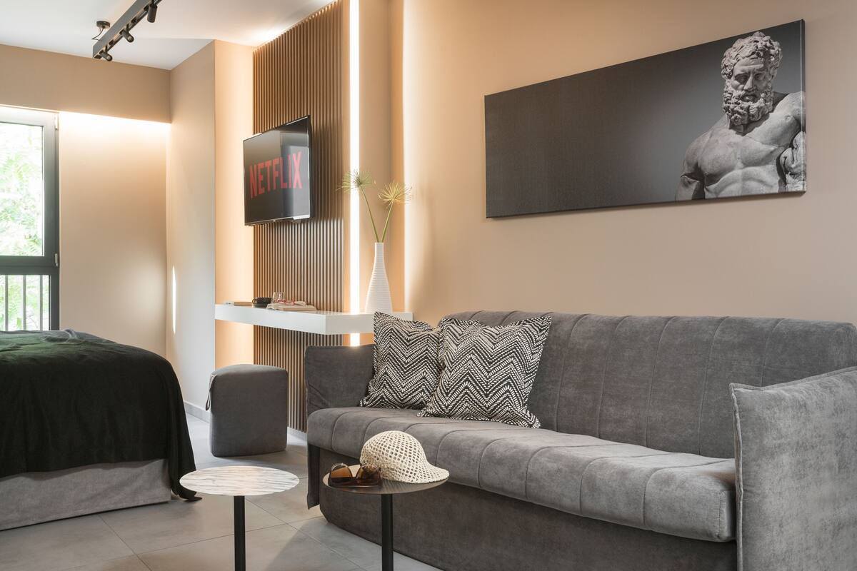 Un salon moderne avec un canapé gris, une petite table ronde, un téléviseur fixé sur un panneau en bois et une statue accrochée au mur.