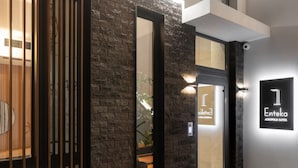 Une entrée d’hôtel moderne avec une façade en pierre, une porte à lattes en bois et une enseigne indiquant « 1 Enteka Acropolis Suites ».