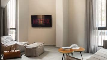 A modern living room with a large flat-screen TV displaying the Netflix logo, a sofa, a coffee table, and a window with curtains.