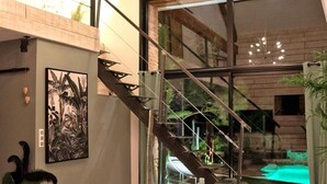 A modern interior with a staircase leading to a balcony, a large window, and a painting on the wall.