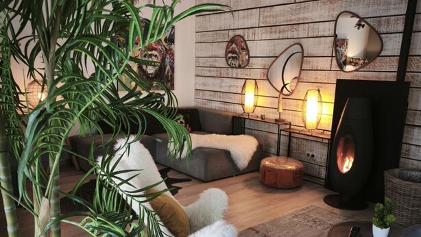 A cozy living room with a sofa, a round ottoman, a side table with a lamp, and a large mirror.