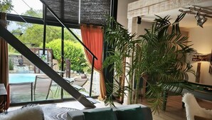 A modern living room with a sofa, a large potted plant, and a view of an outdoor pool area.