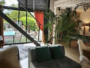 Una sala de estar moderna con un sofá, una planta grande en maceta y vistas a una zona de piscina al aire libre.