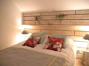 Une chambre à coucher avec une tête de lit en bois, deux lampes de chevet et des coussins à motifs floraux.