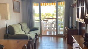 Hyggelig opholdsstue med sofa, spisebord, stole og et køkken med skabe og komfur.