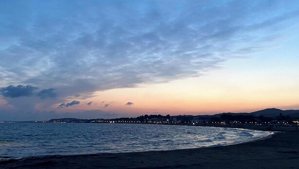 Solnedgang over kysten med strand og by i det fjerne.