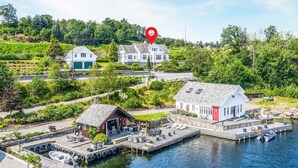 A waterfront property with a dock, a small building with outdoor seating, and a large house with a garage. - Beautiful home in Skjoldastraumen with WiFi (Skjoldastraumen)