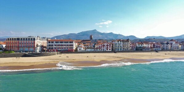 A coastal town with a beach, buildings, and mountains in the background.