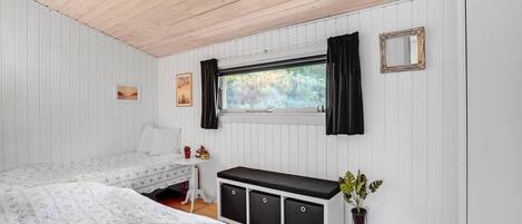 Un dormitorio con dos camas, una ventana con cortinas, un aparador y una planta.