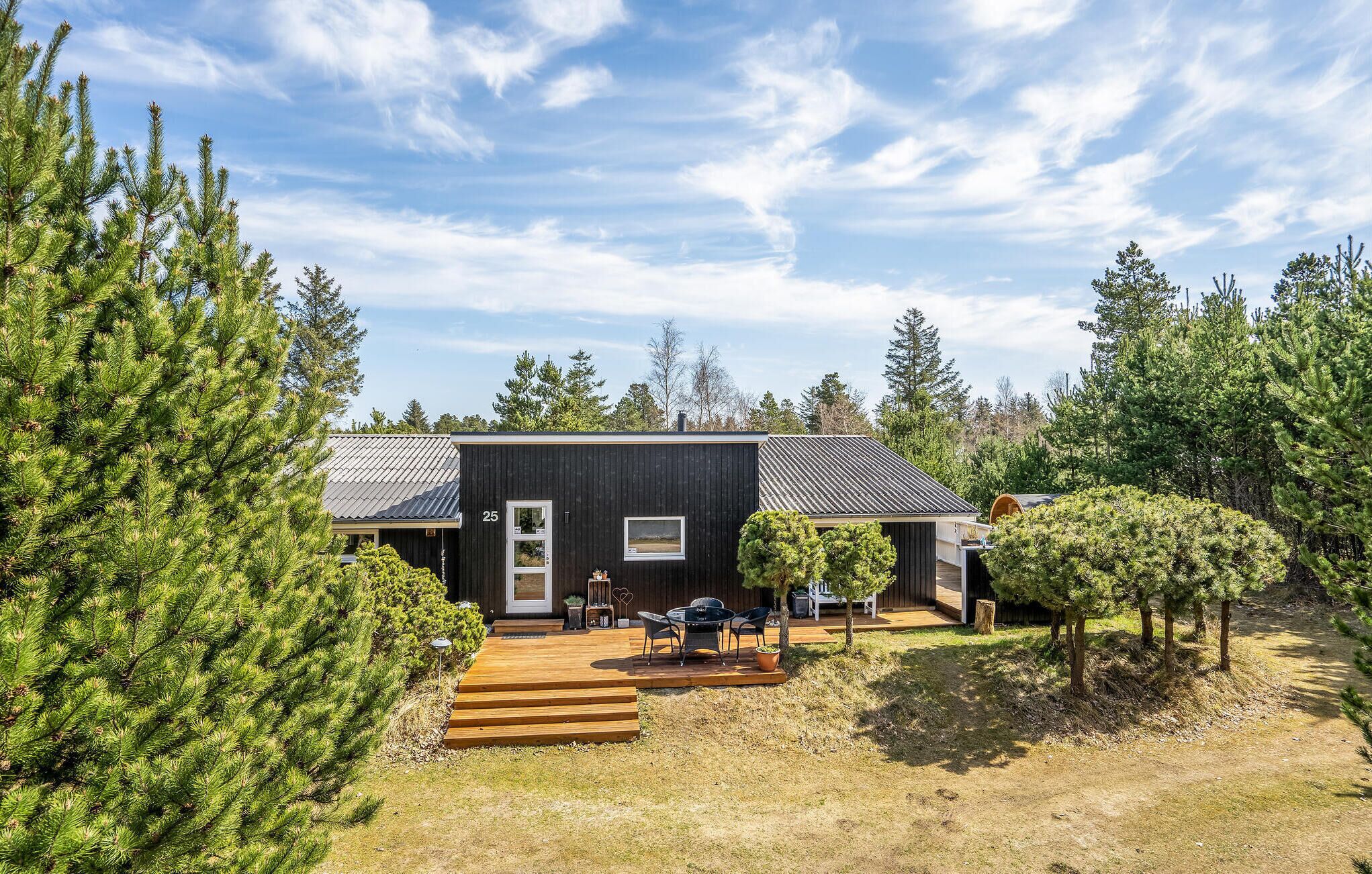 A modern cabin with a dark exterior, a wooden deck, and a small outdoor seating area.