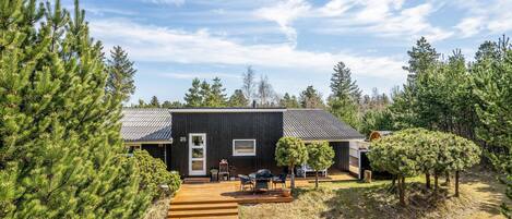 A modern cabin with a dark exterior, a wooden deck, and a small outdoor seating area.