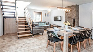 A modern living space with a wooden staircase, a sofa, a dining table with chairs, and a flat-screen TV mounted on the wall. - Gorgeous home in Pasym with sauna (Pasym)