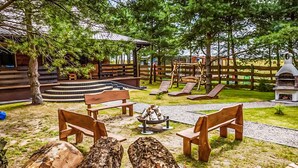 A wooden bench area with a fire pit, surrounded by a wooden deck and a playground with slides. - Gorgeous home in Pasym with sauna (Pasym)