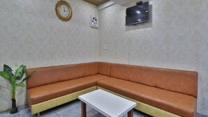 Un salon moderne avec un canapé d’angle marron, une table basse blanche, un téléviseur fixé au mur et une horloge décorative.