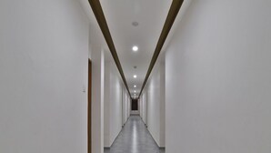 Un long couloir étroit aux murs blancs et au sol carrelé de gris, qui mène à une porte sombre au fond.