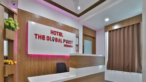 Un comptoir d’accueil d’hôtel avec un revêtement en bois, un plan de travail blanc et une enseigne indiquant « HÔTEL THE GLOBAL POINT ».