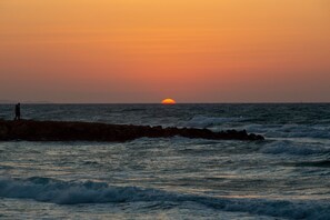 Un coucher de soleil sur l’océan, avec des vagues qui s’écrasent contre une jetée rocheuse.