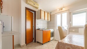 Una cocina funcional con estufa, lavamanos y armarios, una mesa de comedor con mantel, y un ventanal que proporciona luz natural.