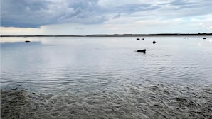 Une étendue d’eau calme, bordée d’une plage de sable, sous un ciel nuageux.