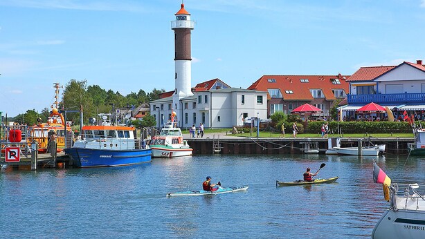 Un port avec des bateaux, un phare et des bâtiments aux toits rouges.