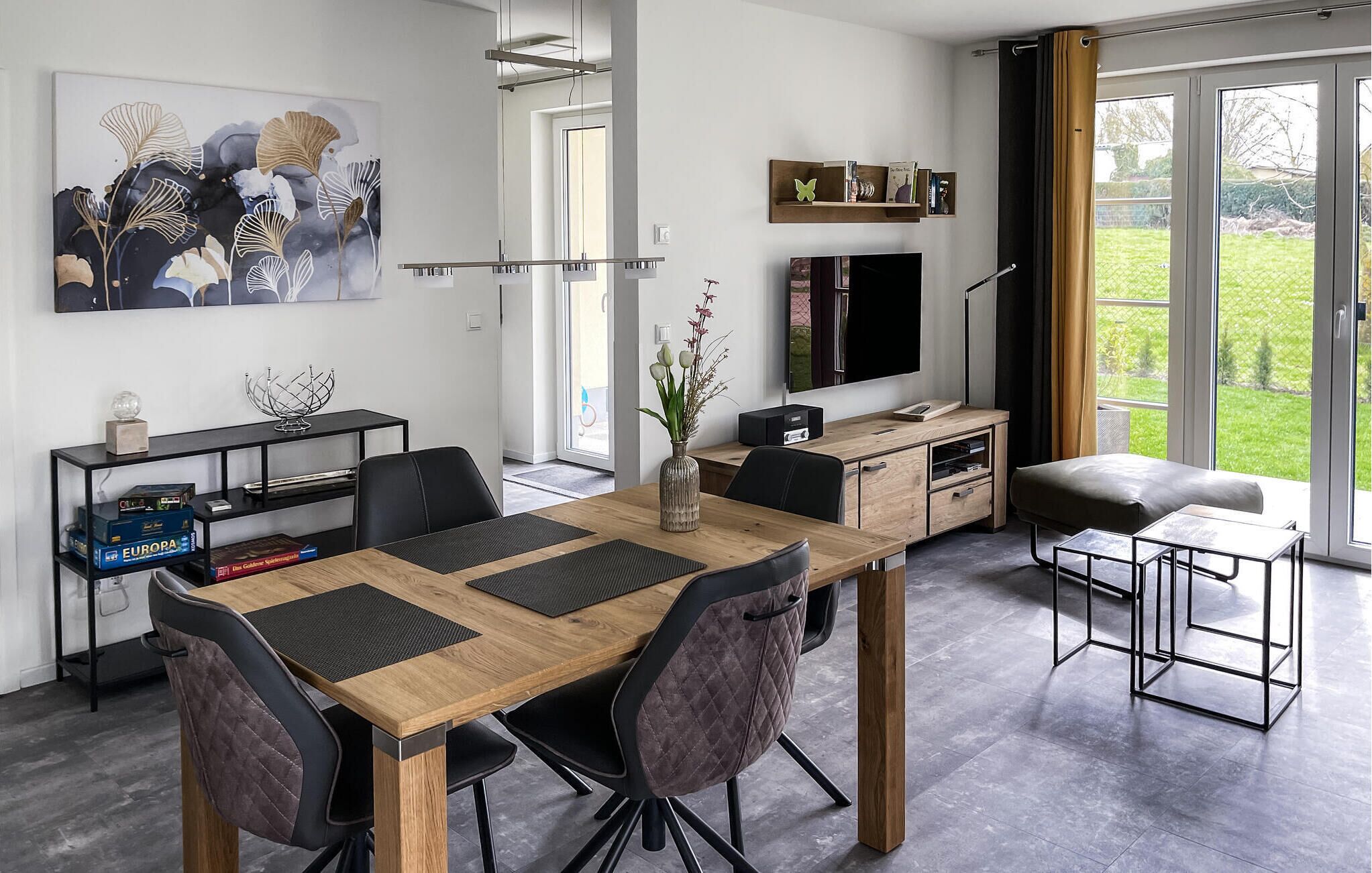 Ett modernt vardagsrum med ett matbord i trä, svarta stolar, en tv och en bokhylla.
