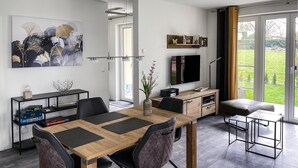 Un salon moderne avec une table à manger en bois, des chaises noires, un téléviseur et une bibliothèque.
