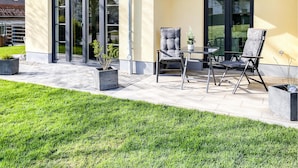 Une terrasse avec deux chaises et une table, une petite plante en pot et une zone herbeuse à l’avant.