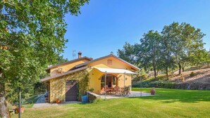 Una casa amarilla con patio, rodeada de árboles y césped.