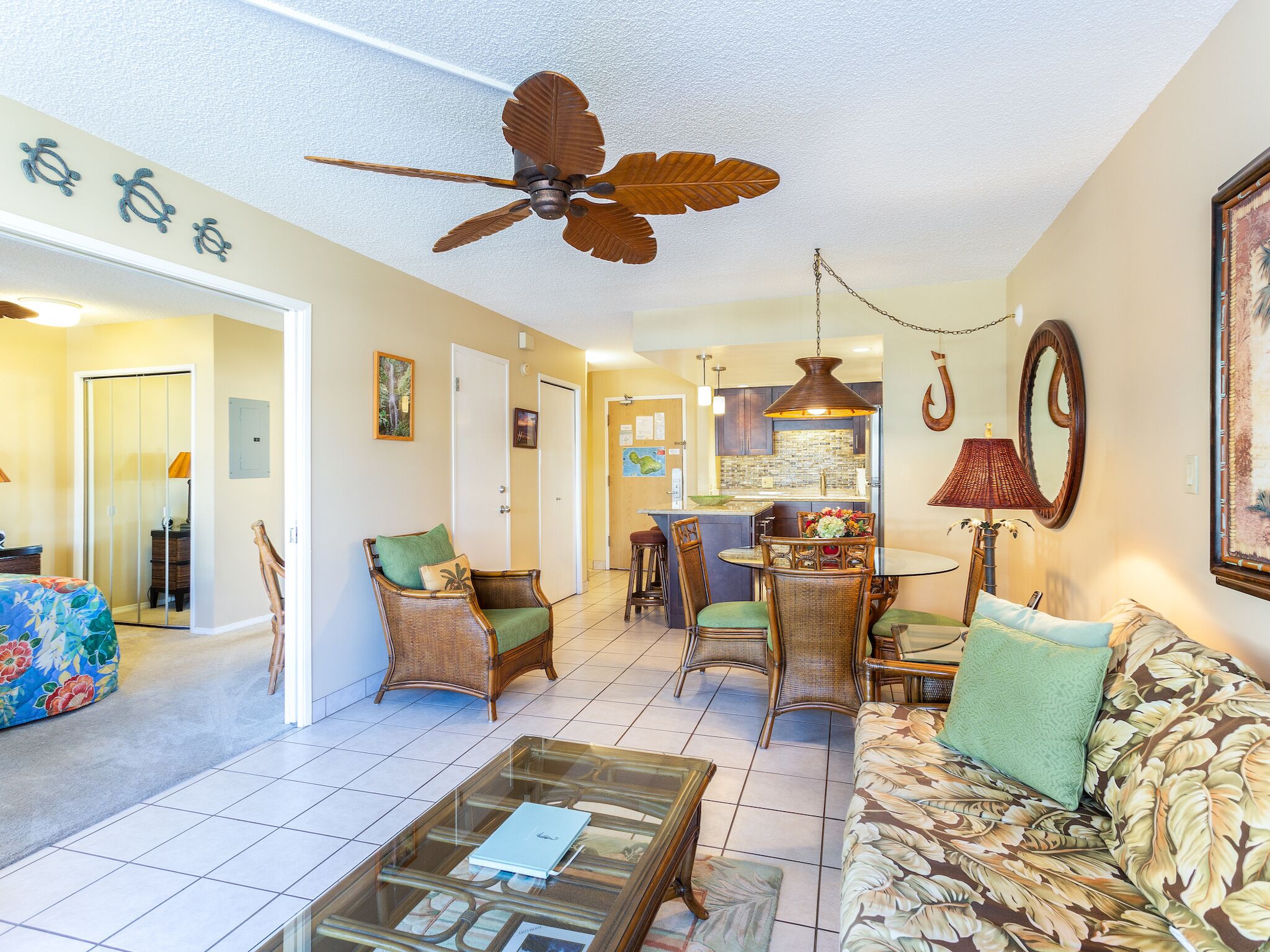 A spacious living room with a ceiling fan, a dining area with wicker furniture, and a kitchen with a tiled backsplash.