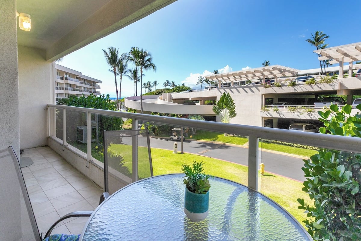 Ein Balkon mit Glastisch, einem Blumentopf und Blick auf einen Parkplatz sowie Gebäude.