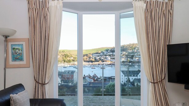 A living room with a black leather sofa, a framed picture on the wall, and a view of a harbor with boats and houses. - 13 Above Town (Dartmouth)