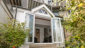 A white house with a large open window, a staircase leading to the entrance, and a garden with various plants. - 13 Above Town (Dartmouth)