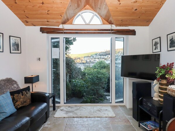 Una sala de estar con un sofá de cuero negro, un televisor y un ventanal con vistas a un pueblo.