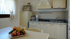 A compact kitchen with white cabinetry, a toaster, a coffee maker, and a fruit bowl on the table.