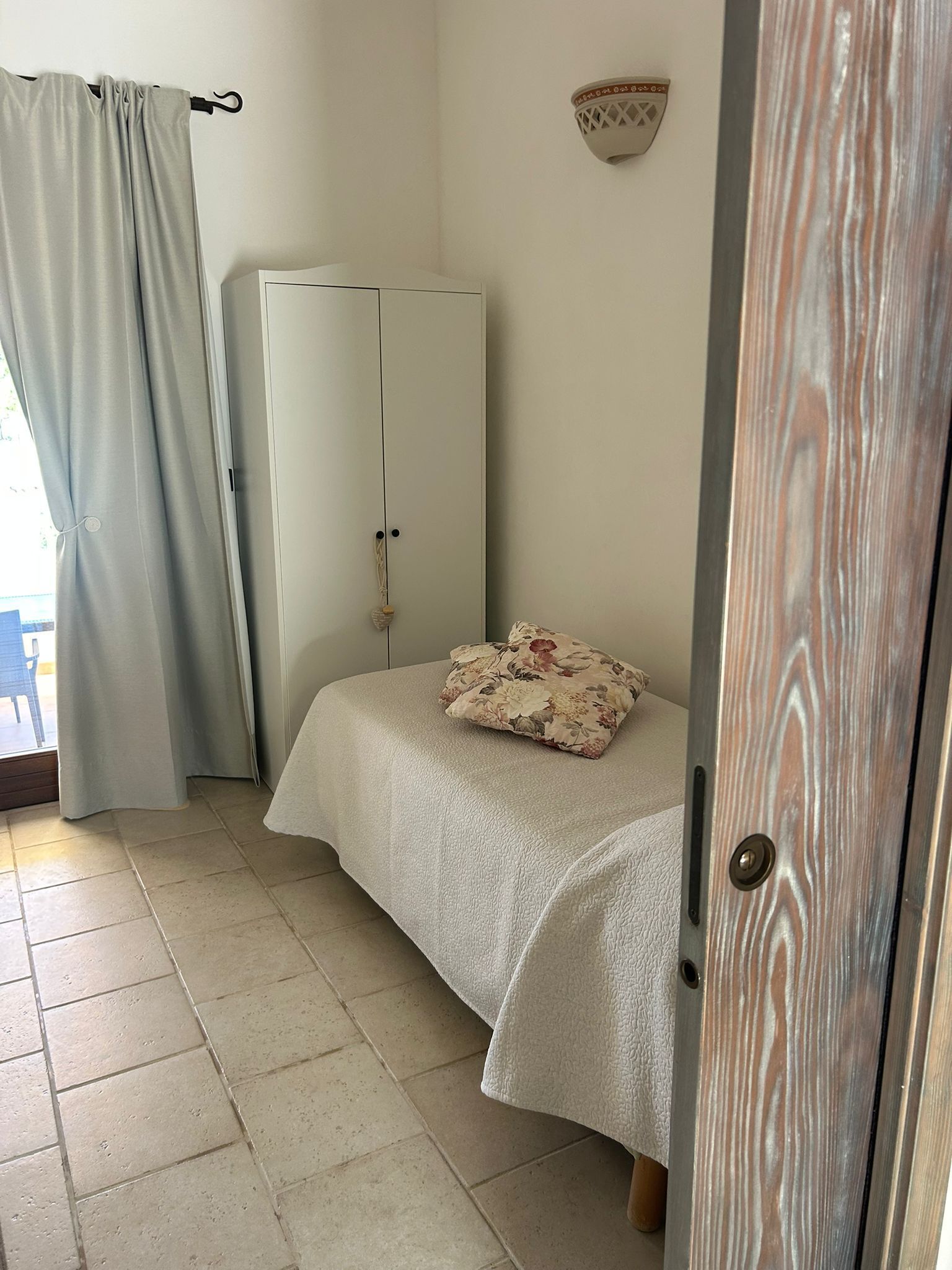 Ett sovrum med en säng, en garderob, ett fönster med gardiner och en väggmonterad lampa.