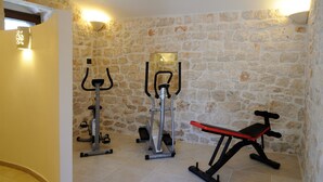 A room with a stone wall, an exercise bike, a bench, and a wall-mounted light fixture.
