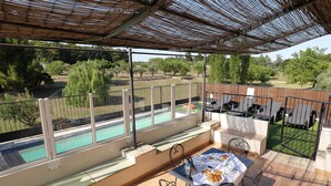 A terrace with a table set for breakfast, overlooking a swimming pool and a garden.