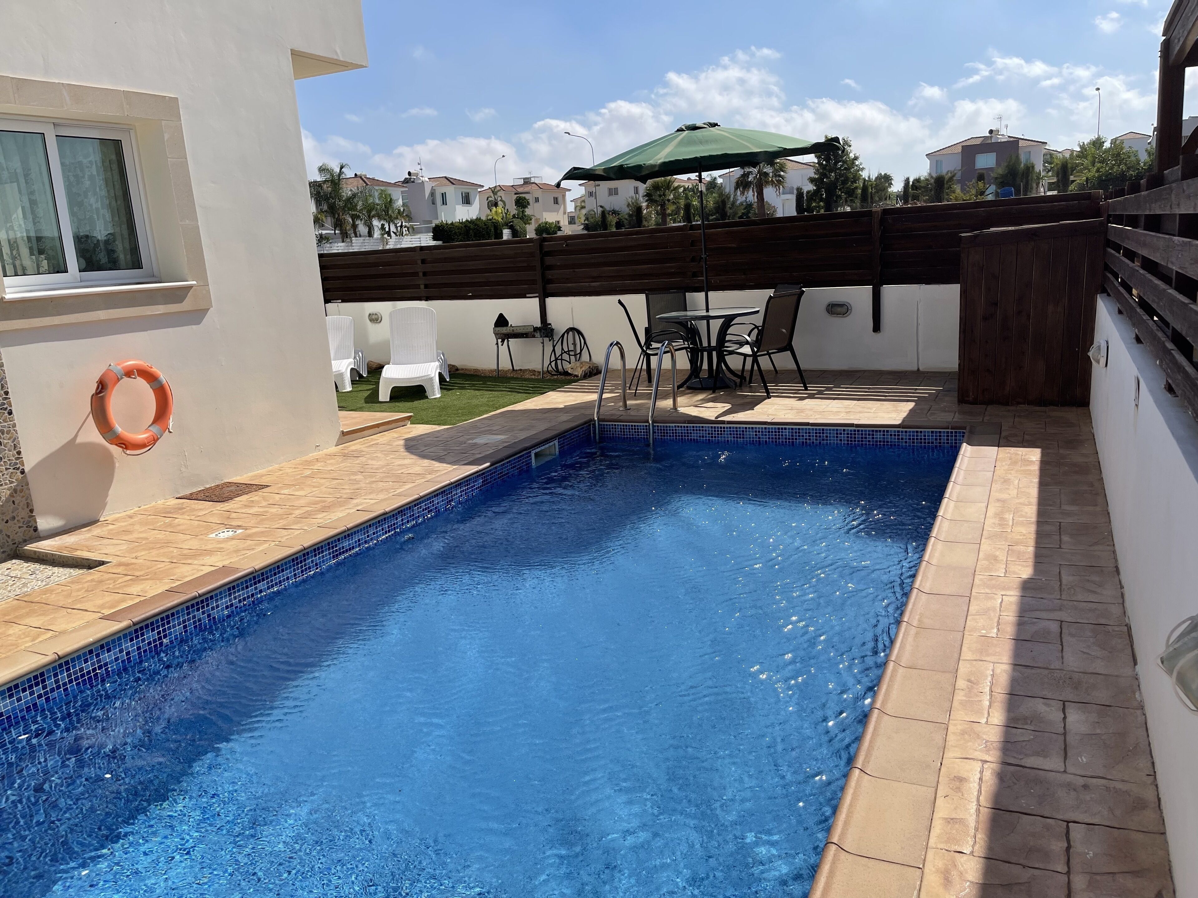 A swimming pool with a tiled edge, a lifebuoy, and a wooden fence.